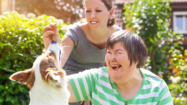 image of an additional needs adult with her dog and a carer